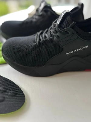 Arbetsskor Skyddsskor med stålhätta nya - Snygga svarta arbetsskor Skyddsskor med stålhätta med ovandel i mesh och texten 'SPORT FASHION' på sidan. Skorna har svarta snören och medföljer gröna, vadderade innersulor för extra komfort. Perfekta för dig som gillar en sportig och stilren look.