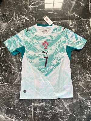 Portugal målvaktströja Puma grön - Snygg Portugal målvaktströja från Puma i ljusgrönt och vitt med vågigt mönster. Tröjan har nummer 1 på framsidan, Portugal-emblemet på bröstet och Puma-logga. Tillverkad i lätt och ventilerande material, perfekt för fotbollsträning eller match.
