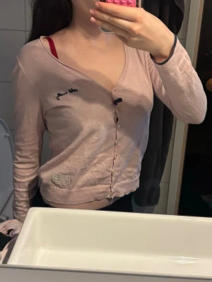 Ljusrosa odd Molly kofta - Söt ljusrosa cardigan med knappar framtill och diskret broderad text vid bröstet. Tröjan har långa ärmar och en mjuk, tunn kvalitet som passar perfekt till lager på lager. Liten etikett nertill och avslappnad passform.