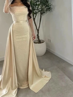 Champagnefärgad långklänning med pärlor - Elegant långklänning i champagnefärg med glittriga pärldetaljer och transparenta långärmar. Klänningen har en markerad midja med satinband och ett långt släp som ger extra lyxig känsla. Perfekt för speciella tillfällen. Storlek 40 men motsvarar 38-36 normalstorlek. Nypris 4000