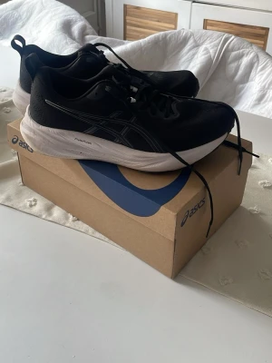 Svarta löparskor från Asics - Snygga svarta löparskor från Asics med vit sula och klassisk logga på sidan. Ovandelen är i mesh för bra ventilation och komfort, och sulan är designad för bra stötdämpning. Perfekta för löpning eller träning. Skorna har snörning och dragflik bak.