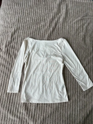 Vit långärmad topp i bomull - En enkel och stilren vit långärmad topp med rak passform. Tillverkad i mjuk bomull som känns skön mot huden. Perfekt att matcha med jeans eller kjol för en clean look. Armarna är 3/4 och bakom visar den en del av ryggen. 