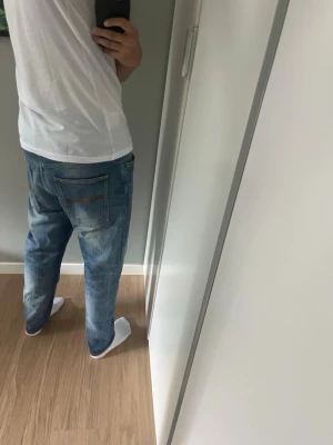 Blåa relaxed Nudie fit jeans herr - Säljer ett par blåa Nudie Brute Knut jeans med relaxed fit och klassisk femficksdesign. Jeansen har en ljus tvätt med slitningar och något lösare passform, perfekta för en chill och avslappnad stil. Passar dig som gillar bekväma och stilrena jeans. W33 men passar W31. Modellen är 179