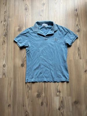 Blå pikétröja från Stone Island - Snygg blå pikétröja från Stone Island med klassisk krage och korta ärmar. Tröjan har en liten logotyp på bröstet och är tillverkad i mjuk bomull. Perfekt för en avslappnad och stilren look. Special modell