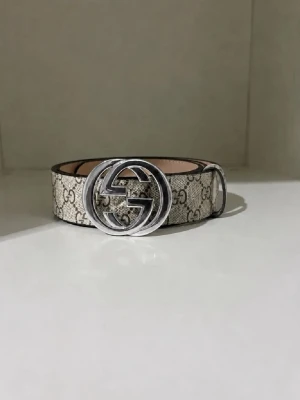 Beige bälte med silverdetalj - Snyggt beige bälte med det klassiska mönstret och en stor, rund silverfärgad spänne. Perfekt accessoar för att lyfta vilken outfit som helst.