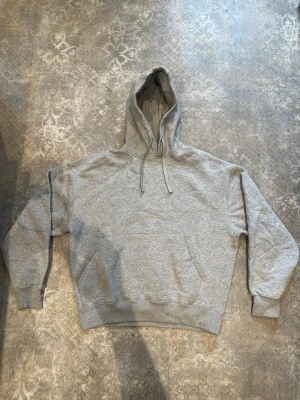 Grå hoodie från Pull&Bear - Klassisk grå hoodie från Pull&Bear med stor känguruficka framtill. Tillverkad i mjukt sweatshirtmaterial som är borstat på insidan för extra komfort. Perfekt för en avslappnad och stilren look.