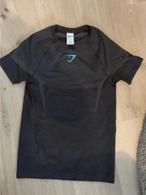 Gymshark onyx v5 - Snygg svart träningströja från Gymshark med korta ärmar och meshpanel upptill för extra ventilation. Tröjan har en diskret logga i turkos på bröstet och är tillverkad i ett lätt och stretchigt funktionsmaterial som passar perfekt till gymmet eller löpning. Tröjan är exklusiv gymshark och ifrån droppet av onyx v5 som är svår att få tag på. Aldrig använd