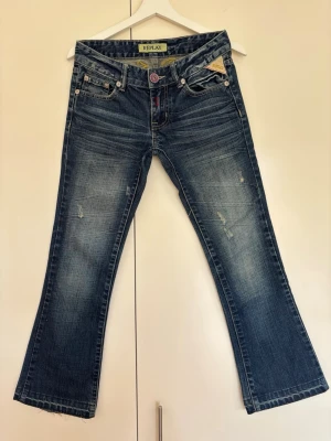 Blå bootcut lowrise  jeans från Replay - Grymt snygga blå bootcut jeans från Replay med låg midja, slitna detaljer och broderad logga bak. Klassisk femficksmodell med låg midja och utsvängda ben. Jeansen har coola kontrastsömmar och är gjorda i mjuk denim. Mått waist (låg) 78 cm, innerbensmått 71 cm