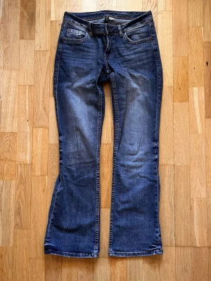Mörkblå bootcut jeans stl 40 - Säljer ett par mörkblå bootcut jeans med klassisk femficksdesign och lätt slitningar framtill. Jeansen har normal midja och dragkedja med knapp bakfickor med lock.. Materialet är denim i bomull med lite stretch för skön passform. Var för stora för mig så sparsamt använda. 