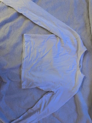 Vit långärmad topp från 157 - En basic vit långärmad topp från 157 i mjuk bomullsblandning med lite stretch. Enkel och clean design med rund halsringning, perfekt att styla med jeans eller kjol. Materialet är 95% bomull och 5% elastan för en skön passform.