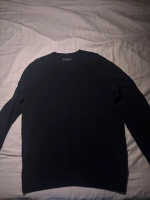Mörkblå stickad tröja Marc O'Polo - Snygg mörkblå stickad tröja från Marc O'Polo med rund halsringning och diskret struktur i materialet. Perfekt för lager-på-lager och enkel att matcha med jeans eller chinos. Klassisk modell med ribbade muddar vid ärmslut och nederkant.