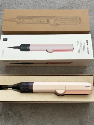 Dyson Airstrait hårstyler rosa - Säljer en Dyson Airstrait hårstyler i en snygg ljusrosa färg med svarta detaljer. Verktyget har en modern, avlång form och är tillverkat i plast och metall. Perfekt för att styla håret snabbt och smidigt med innovativ teknik.