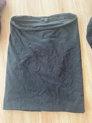 Svart enkel kortkjol - En svart, enkel och rak kortkjol i mjukt bomullsmaterial. Kjolen har en minimalistisk design utan synliga detaljer och passar perfekt till en avslappnad eller stilren outfit.