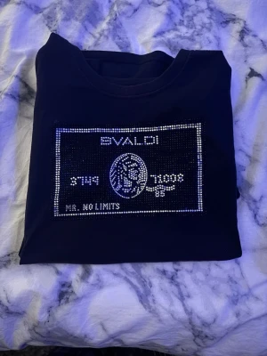 Svart t-shirt med glittrig print - Svart t-shirt från bvaldi  med glittrig print framtill som liknar ett kreditkort. T-shirten har rund halsringning och korta ärmar. Perfekt för dig som vill sticka ut med en unik och snygg detalj på bröstet.