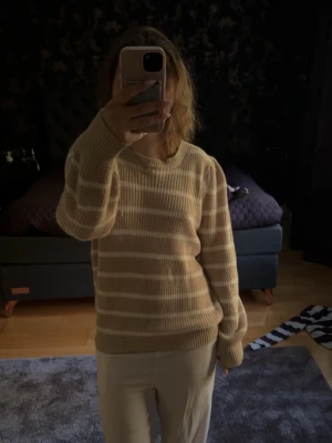 Stickad tröja - Mysig stickad tröja i beige med vita horisontella ränder. Tröjan har rund halsringning, långa ärmar och ribbade muddar vid ärmslut och nederkant. Perfekt för lager på lager och en avslappnad stil.