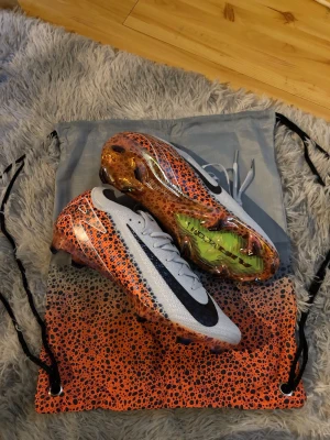 Nike Mercurial ÖPPET FÖR ALLA BUD - Snygga Nike Mercurial fotbollsskor i vitt och orange med svart swoosh och coolt prickigt mönster. Skorna har en strömlinjeformad design och är tillverkade i lätt syntetmaterial för bästa känsla på planen. Levereras med matchande påse.