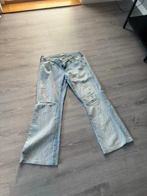 Ljusa slitna jeans från Gina Tricot Young  - Säljer ett par ljusblå jeans från Gina Tricot Young med raka ben och slitningar på både lår och knän. Jeansen har klassisk femficksmodell och är tillverkade i denim. Perfekta för en avslappnad och trendig look. Knappt använda. Uppsydda, passar längd 158 cm
