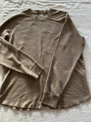 Beige långärmad tröja från Zara - En beige långärmad tröja från Zara i mjukt, ribbat material. Tröjan har rund halsringning och avslappnad passform, perfekt för en chill och enkel stil. Passar till jeans eller mjukisbyxor för en casual look.