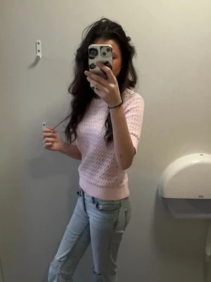 Ljusrosa stickad topp med kort ärm - Söt ljusrosa stickad topp med korta ärmar och hålmönster. Modellen är croppad och har ribbade kanter vid ärmslut och midja. Perfekt för vår och sommar, enkel att styla med jeans eller kjol.