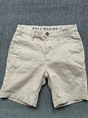 Beige shorts från Race Marine XS - Snygga beige shorts från Race Marine i klassisk modell med normal passform. De har bälteshällor, knapp och dragkedja framtill samt två sidofickor. Perfekta för varma dagar och enkla att matcha med olika stilar.