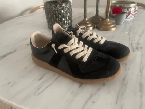 Svarta sneakers med beige sula - Snygga svarta sneakers med beige sula och vita snören. Skorna har en klassisk låg siluett och är tillverkade i en mix av mocka och läder. Perfekta för dig som gillar stilrena och tidlösa sneakers med en retrovibe. Passar no runt 42 43. Användet dom 3 gånger passar ej mig 