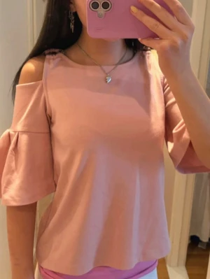 Ljusrosa topp med volangärm - Superfin ljusrosa topp med offshoulder och volangärmar. Toppen har en lös passform och är tillverkad i mjukt bomullstyg. Perfekt för dig som gillar en söt och trendig stil.