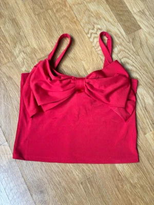 Croptop med rosett - Supersöt Croppad topp med rosett. 44,5 cm från axelbanden. Ny med prislapp.