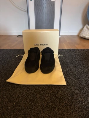 Svarta sneakers från Axel Arigato - Säljer ett par svarta sneakers från Axel Arigato. Skorna har en chunky sula och är tillverkade i mocka med minimalistisk design. Perfekta för dig som gillar stilrena och moderna sneakers. Levereras med originalpåse och box.
