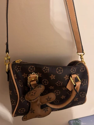 Brun axelväska med monogrammönster - Snygg brun axelväska med guld detaljer. Använd max 4 gånger 