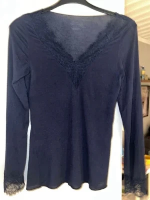 Mörkblå långärmad tröja från intimissmi - Snygg mörkblå långärmad topp med v-ringning och spetsdetaljer både vid halsringningen och vid ärmsluten. Perfekt att styla med jeans eller kjol för en trendig look. Den har ett litet hål på ena armen men inget man märker pris kan diskuteras 