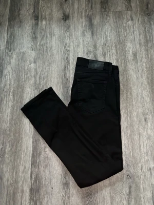 Slim glen jeans svart - Snygga svarta slim fit jeans med klassisk femficksdesign och raka ben. Jeansen har bälteshällor och knappgylf. Perfekta för dig som gillar en stilren och enkel look.