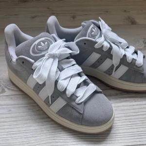 Adidas Campus 00s Grey - Säljer ett par Adidas Campus 00s i den klassiska grå färgen med vita detaljer.                             Storlek: EU 44 / US 10 Modell: Campus 00s      Färg: Grey Three/Cloud White/Off White                                                   Skick: Oanvända/nyskick, Originalkartong: Ja Skorna är i mycket fint skick utan synligt slitage. Sulorna är helt rena, se bilder. Originalkartong medföljer.  Säljer då de inte kommer till användning.