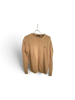 Ralph lauren tröja  - Snygg beige stickad tröja med rund halsringning och ribbade muddar. Tröjan har en liten broderad logga på bröstet och är perfekt för lager på lager. Passar till både jeans och kjol för en avslappnad look.
