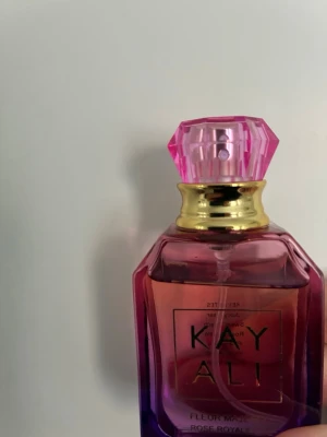 Kayali Fleur Majesty Eau de Parfum 30 ml - Säljer en Kayali Fleur parfym i en snygg glasflaska med gradient från rosa till lila och guldigt detaljerad hals. Flaskan har en multifacetterad rosa kork som ger en lyxig känsla. Perfekt för dig som gillar blommiga och fräscha dofter.