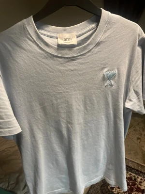 Ljusblå t-shirt från Ami - Snygg ljusblå t-shirt från Ami med klassisk rund halsringning och diskret broderad logga med hjärta och A på bröstet. Tillverkad i mjuk bomull och har en enkel, clean look som passar till det mesta.