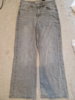 Grå raka jeans från Gina Tricot  - Säljer ett par grå jeans med rak passform och rå kant nertill. Jeansen har klassisk femficksdesign, bälteshällor och knappgylf. Perfekta för en avslappnad och trendig look. Materialet är denim i bomull.