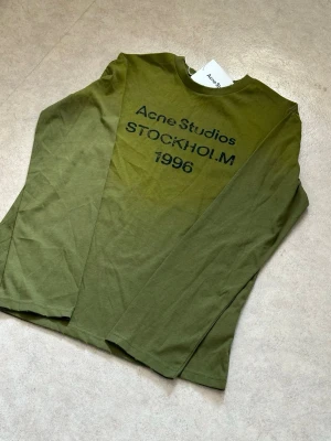 Grön långärmad tröja Acne Studios - Snygg grön långärmad tröja från Acne Studios med tryck 'STOCKHOLM 1996' på bröstet. Tillverkad i mjuk bomull och har en avslappnad passform. Perfekt för dig som gillar minimalistisk och stilren design.