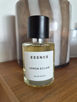 ESSNCE Lemon Eclair Eau de Parfum - Fräsch parfym från ESSNCE med doften Lemon Eclair. Kommer i en rund glasflaska med svart lock och vit etikett. Parfymen har en ljusgul färg och modern, minimalistisk design som passar perfekt för dig som gillar citrusdofter.