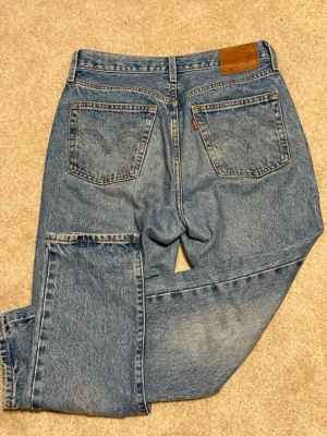 Blå raka jeans från Levis - Klassiska blå jeans i rak modell med hög midja och fem fickor. Jeansen har en ljus tvätt och tydliga sömmar på bakfickorna samt en brun patch i midjan. Materialet är kraftig denim i 100% bomull.