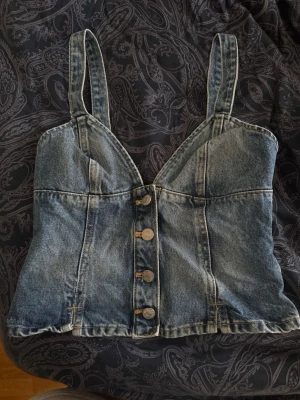 Zara Denim topp - Säljer en snygg denim korsettopp med breda axelband och knappar framtill. Toppen har en figurnära passform och smockad rygg för extra komfort. Perfekt till sommaren eller utekväll och lätt att styla med olika outfits.