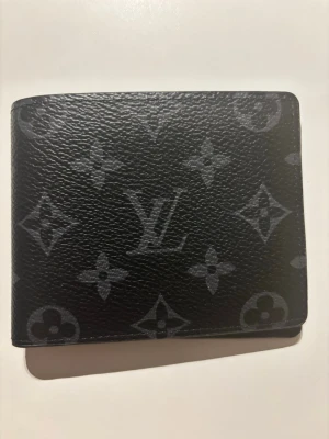 Svart plånbok  - Snygg svart plånbok från H&M i klassiskt monogrammönster. Tillverkad i präglat läder med diskret H&M -logga och ikoniska blommor i grått. Perfekt storlek för kort och sedlar, stilren och lyxig design.