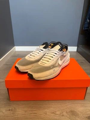 Nike Waffle One sneakers i vit och grå - Säljer ett par Nike Waffle One skor 👟! Skorna är i storlek 44 men passar bättre med folk med storlek 43📏!  Skorna är i ett mycket fint skick och inte använda särskilt mycket!✅ Skriv vid funderingar!✅ postar inom 24h🚚📦!