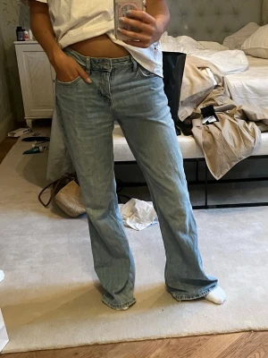Ljusblåa flare jeans - Säljer ett par ljusblå jeans med rak passform och hög midja. Jeansen har klassisk femficksdesign och långa ben som faller snyggt över skorna. Perfekta för en avslappnad och trendig look.