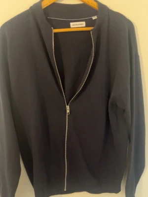 Jack & Jones zip tröja - Mörkblå hoodie från Jack & Jones med hel dragkedja framtill. Klassisk modell med långa ärmar och mjukt material. Perfekt för en avslappnad stil och enkel att matcha med andra plagg.