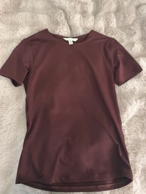Mörkröd basic t-shirt - En enkel mörkröd t-shirt med rund hals och korta ärmar. T-shirten har en slim fit passform och är tillverkad i ett mjukt, stretchigt material som känns skönt mot huden. Perfekt att matcha med jeans eller kjol för en clean look.