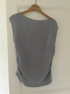 Ljuslila strukturerad topp - Säljer en ljuslila topp med vågig struktur och lös passform. Toppen har bred halsringning och är ärmlös, vilket ger en avslappnad och modern look. Materialet är stretchigt och mjukt, perfekt för en trendig vardagsstil.