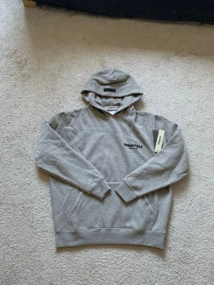 Grå Essentials hoodie  - Snygg grå hoodie från Essentials. Passar dig som är 178 till 187