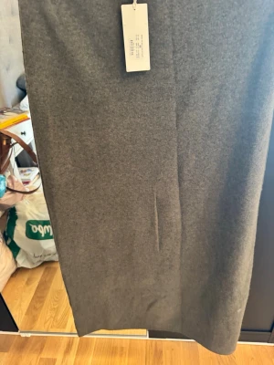 Khaki lång kjol i ullmix - En stilren grå kjol i rak modell med lång längd. Kjolen är tillverkad i en mjuk ullmix som ger en exklusiv känsla och passar perfekt till olika outfits. Enkel design utan synliga detaljer för en clean look.