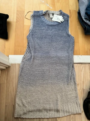 Ärmlös stickad klänning i grått - Stickad ärmlös klänning med rund halsringning och snygg ombre-effekt från mörkgrått upptill till ljusgrått nedtill. Sidorna har ett öppet stickat mönster som ger en cool detalj. Perfekt att styla med en långärmad topp under.