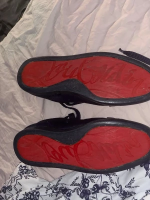 Blåa sneakers från Christian Louboutin - Snygga blå sneakers i mocka från Christian Louboutin med klassisk röd sula och diskreta sömdetaljer. Skorna har lågt skaft, rund tå och matchande blå skosnören. Insidan är ljusbeige och sulan har den ikoniska Louboutin-signaturen.